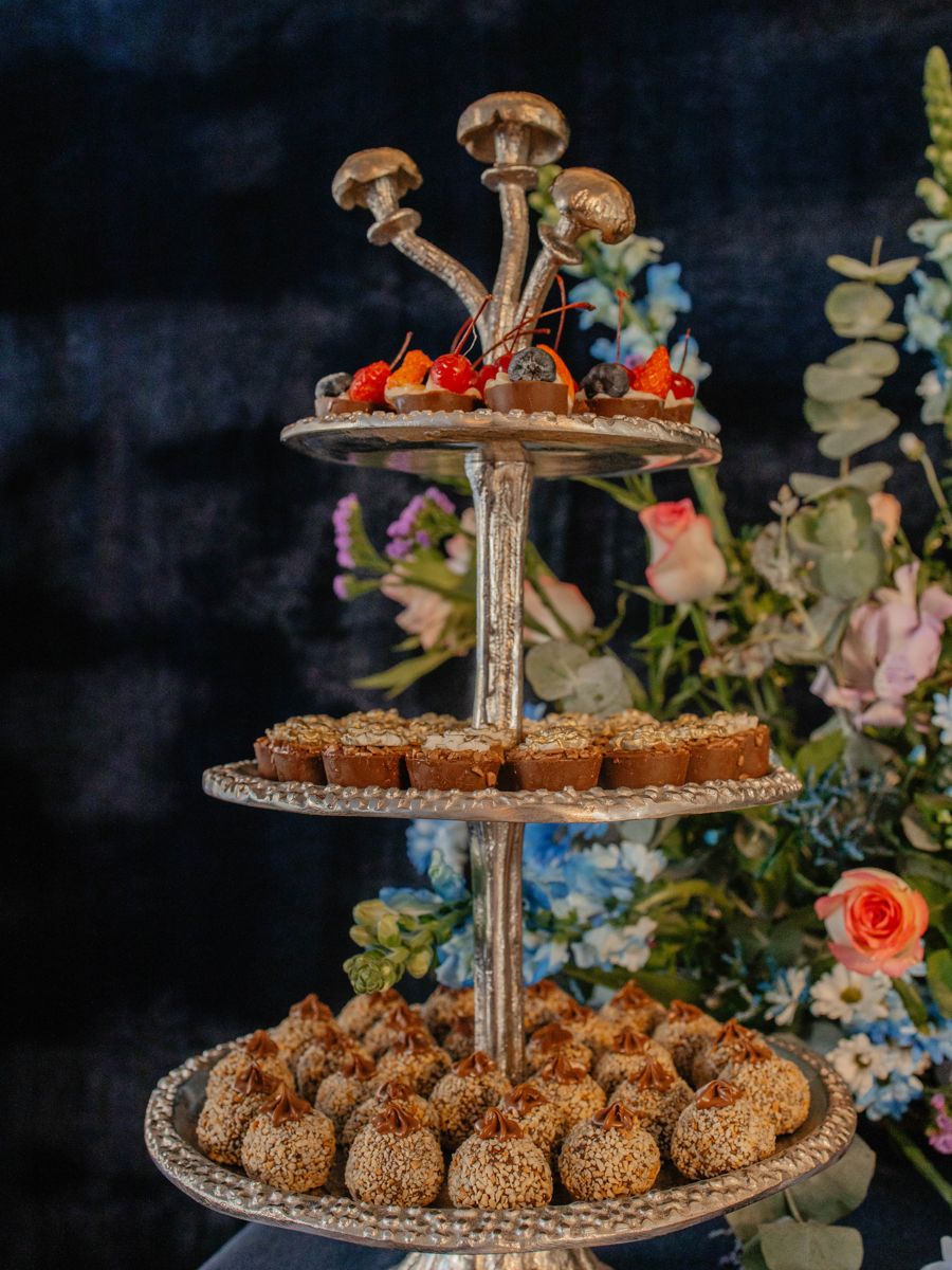 Torre de três andares com docinhos, cercada de flores azuis, rosas e lilás