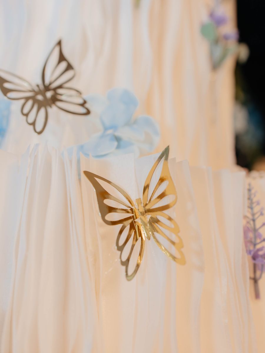 Detalhe do bolo branco com borboletas douradas e flores azuis
