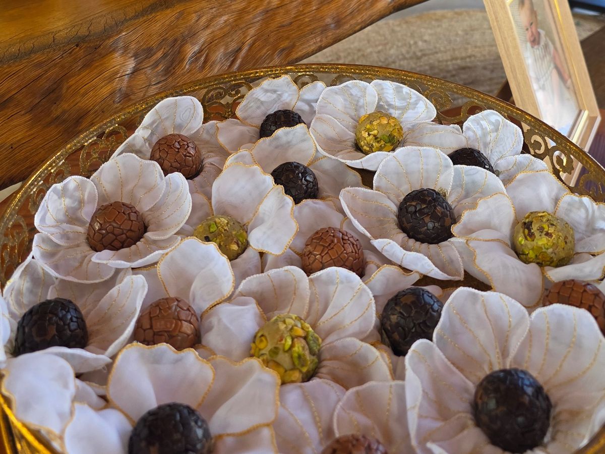Doces de chocolate em forminhas de pétalas brancas, numa bandeja dourada