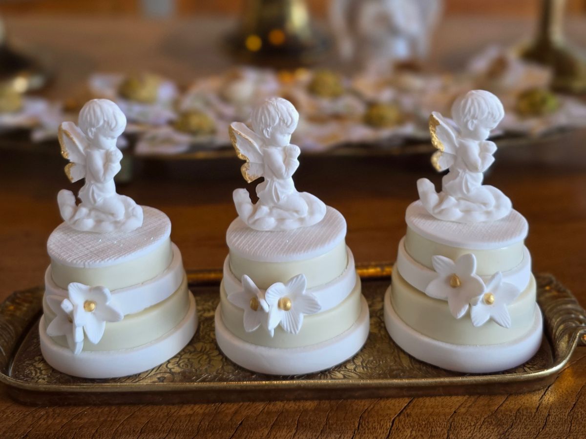 Três minibolos brancos com anjinhos e flores de açúcar, sobre uma bandeja dourada