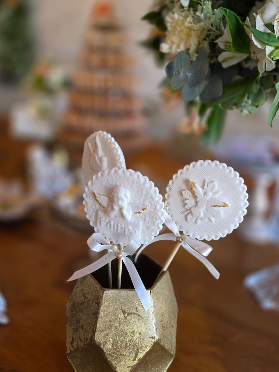 Pirulitos de biscuito brancos com anjinhos, em um vaso dourado sobre a mesa