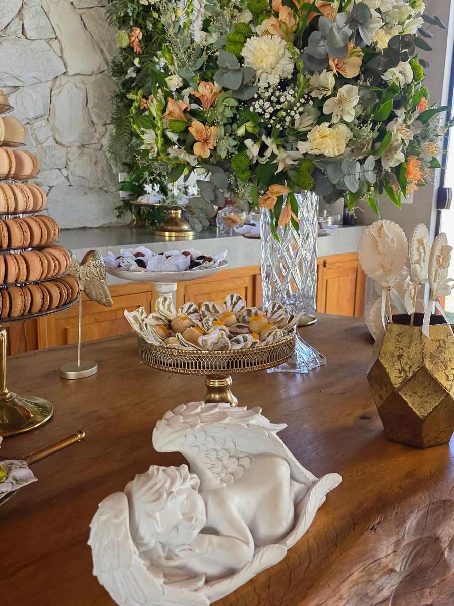 Anjo de gesso deitado sobre a mesa de madeira, com um arranjo de flores ao fundo