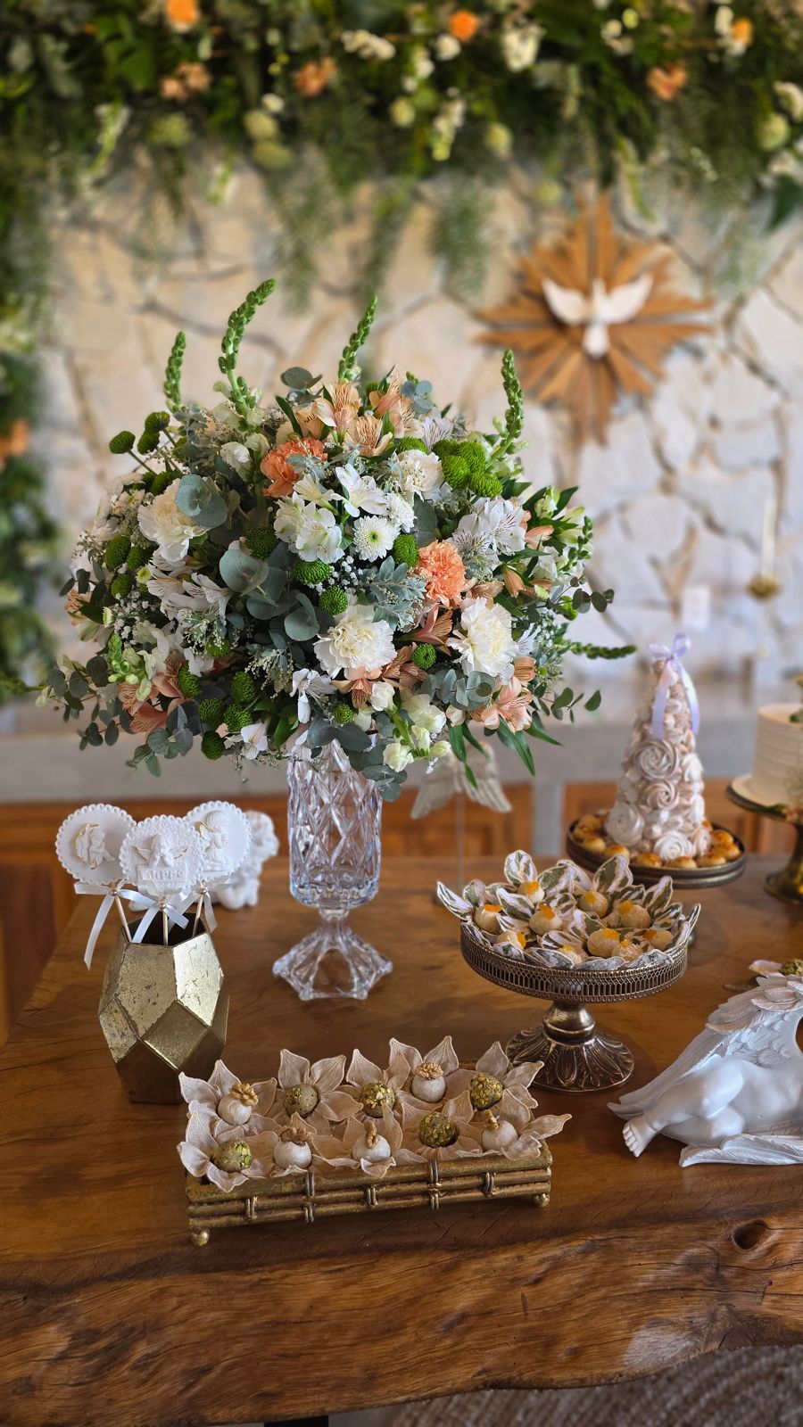 Arranjo de flores, pirulitos e docinhos, sob a pomba do Espírito Santo.