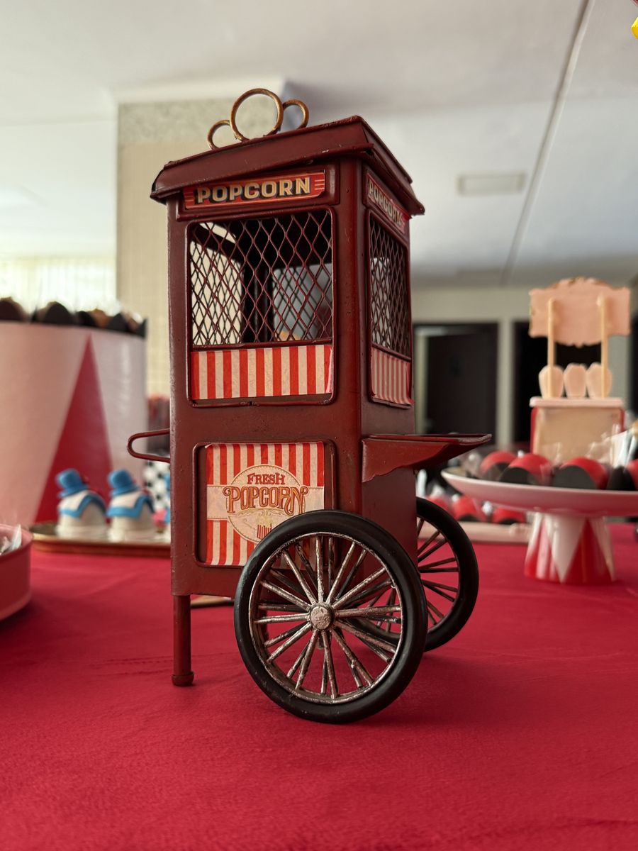 Carrinho de pipoca vermelho em miniatura sobre a toalha vermelha da mesa de doces