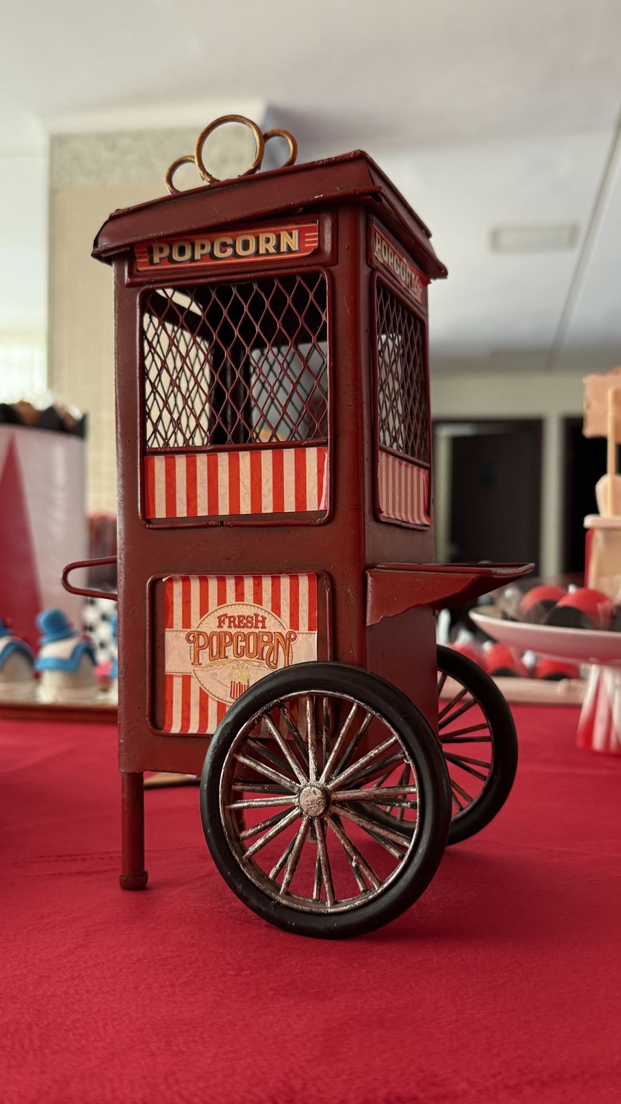Um carrinho de pipoca em miniatura sobre a toalha vermelha.