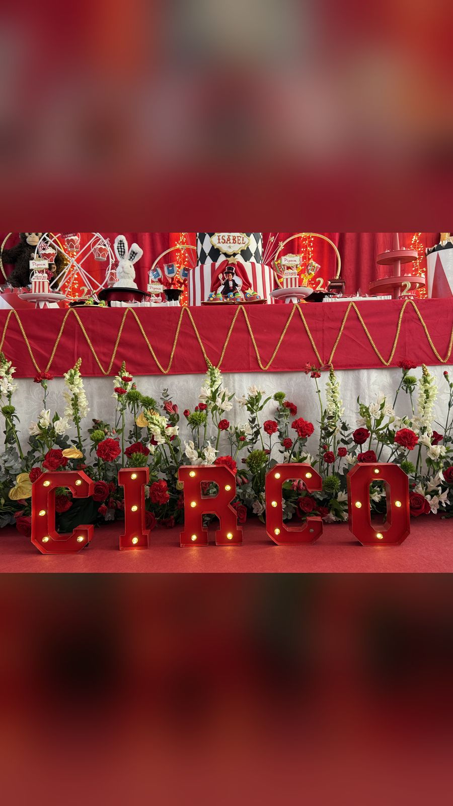 O letreiro CIRCO aceso entre rosas vermelhas e flores brancas.